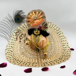 Laddu Gopal idol dressed in a cream and gold outfit with intricate pearl detailing, holding a flute and surrounded by rose petals.